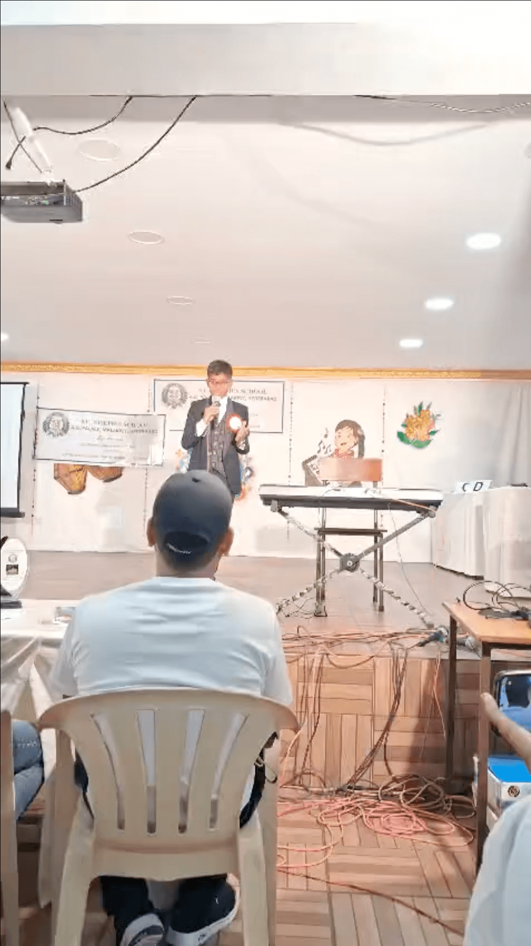Bala standing on a stage holding a microphone, with a keyboard on a stand beside him and a listener seated in front.